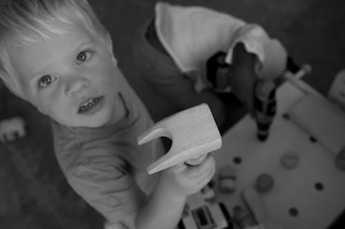 Greyscale Photo of Boy on Tshirt Holding Brown Wood