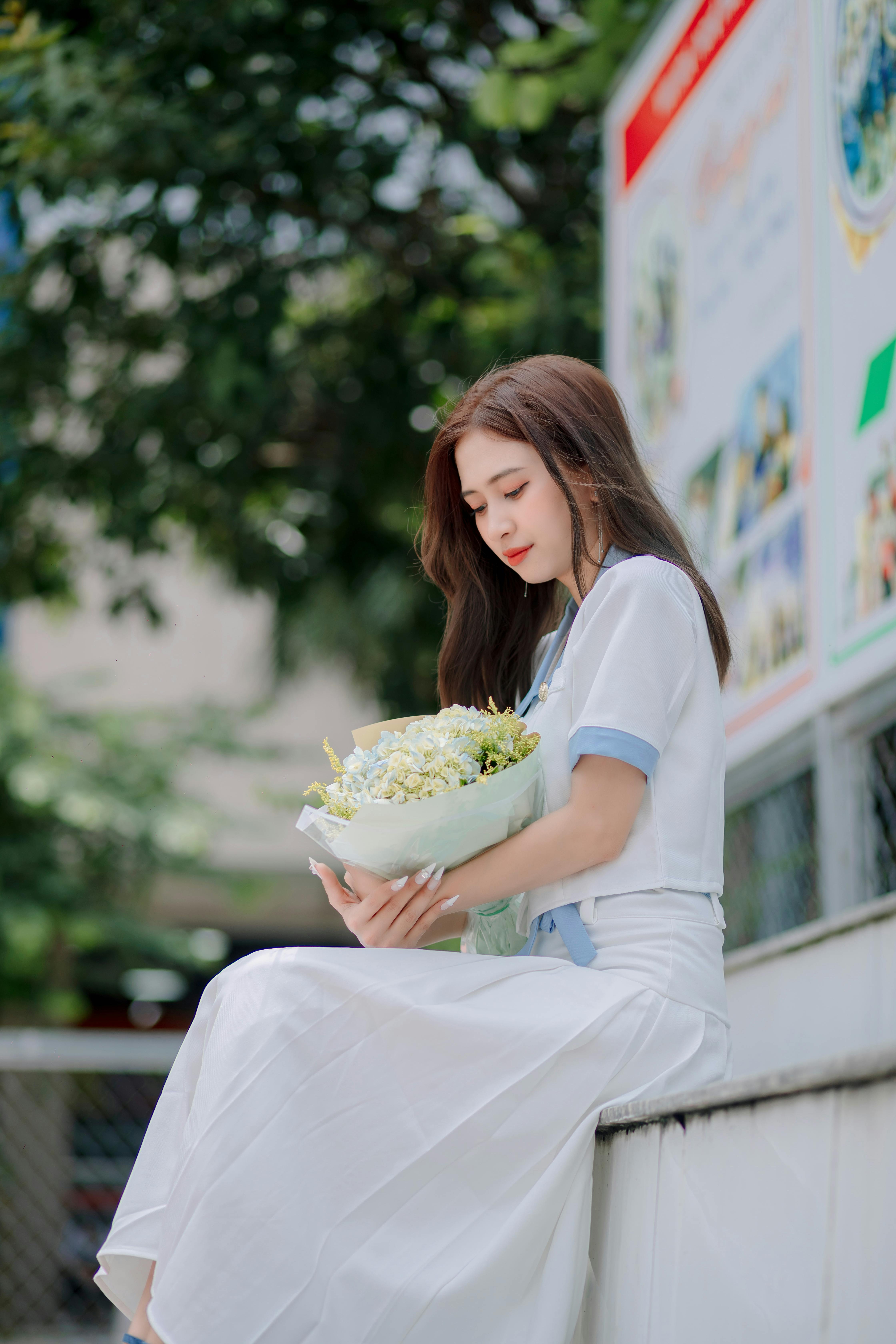 Young Woman in White Blouse and Maxi Skirt Holding a Flower