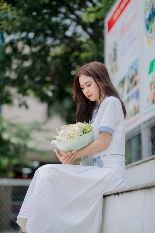 Young Woman in White Blouse and Maxi Skirt Holding a Flower Bouquet