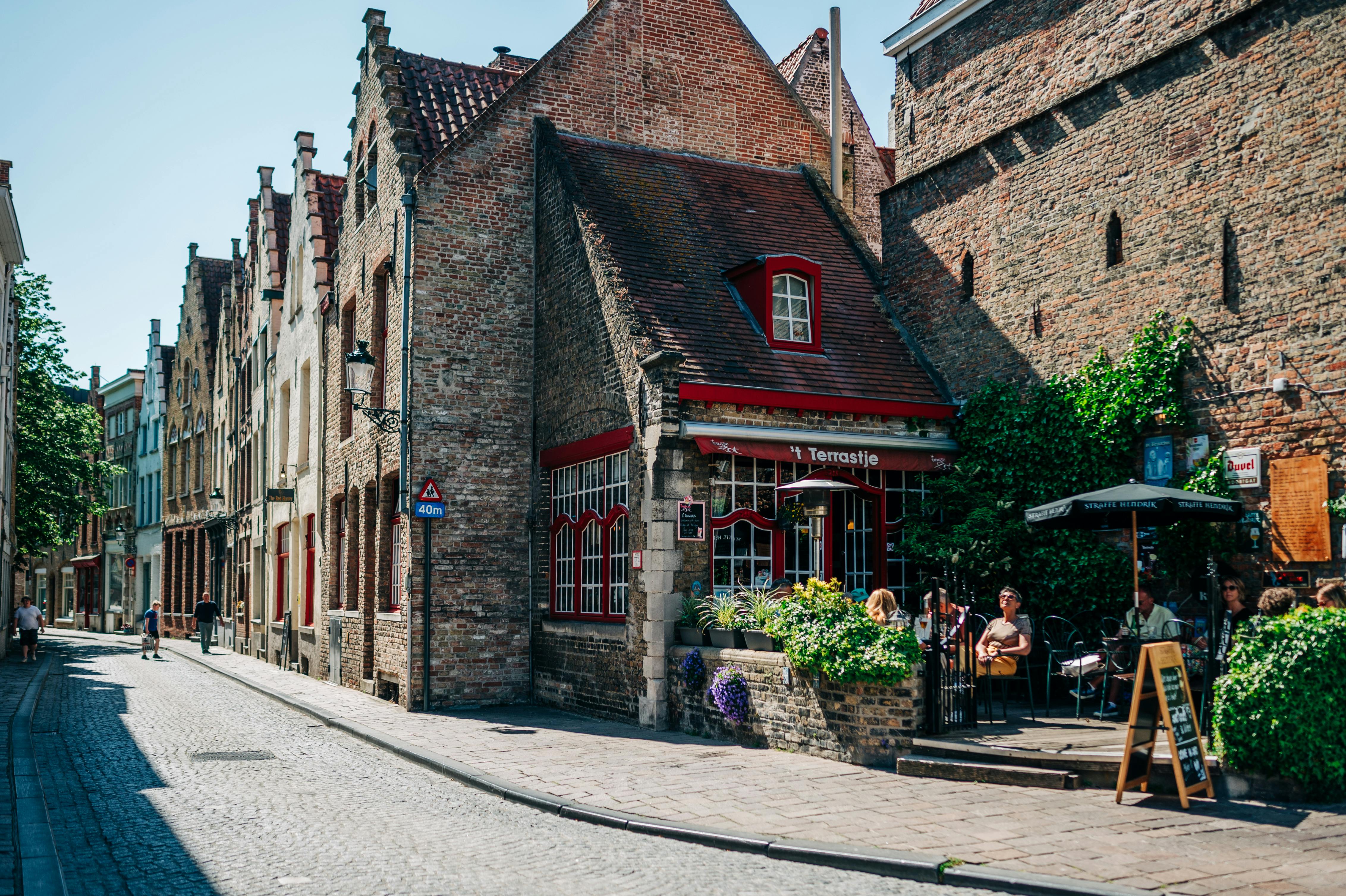 fascia blasting benefits cellulite reduction - Cozy café amidst historic buildings on a cobblestone street in Bruges, Belgium, under sunny skies.