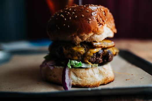 Close-up of a juicy cheeseburger with lettuce, red onion, and sauce on a rustic tray.