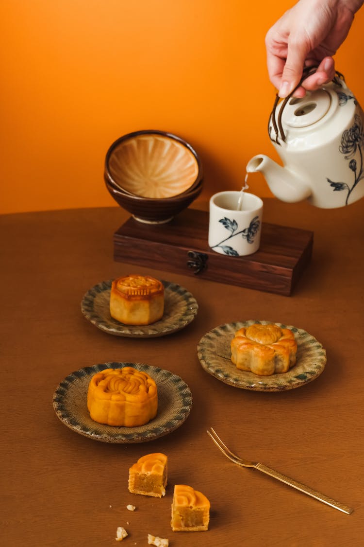 Woman Hand Pouring Water From Kettle To Cup Near Cakes On Plates