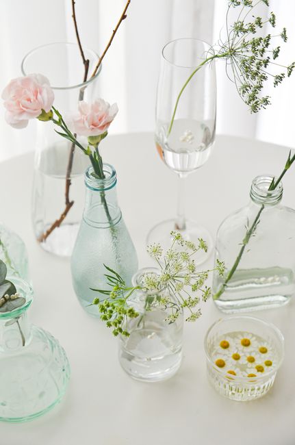 Delicate flowers in clear glass vases on a white table in natural light, creating an elegant minimalist scene.