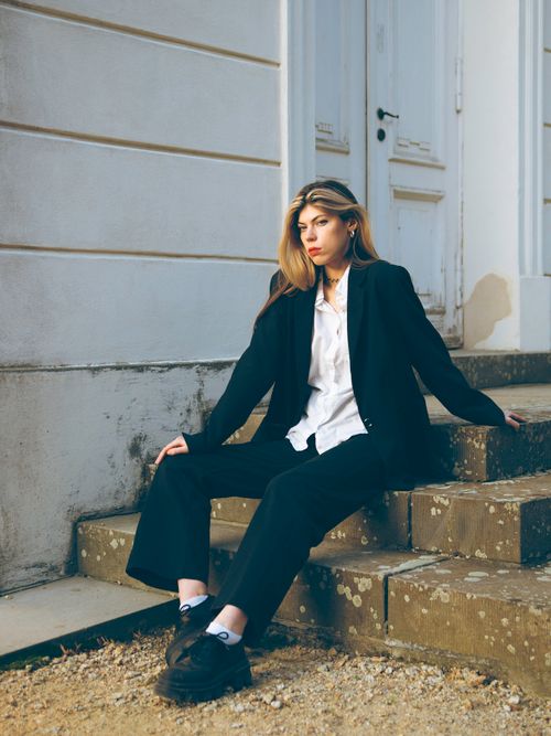 Free Fashionable woman in a black blazer and pants sitting on steps, showcasing urban style in Berlin. Stock Photo