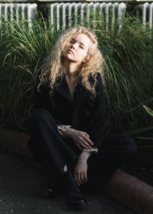 Beautiful Blonde Woman in Jacket Sitting on Ground in Garden