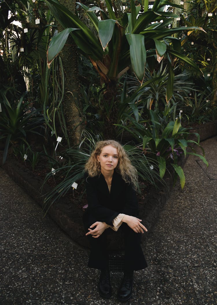 Beautiful Blonde Woman Sitting In Front Of The Plants