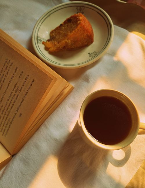 Free Warm morning light over a cup of coffee, cake slice, and an open book. Stock Photo