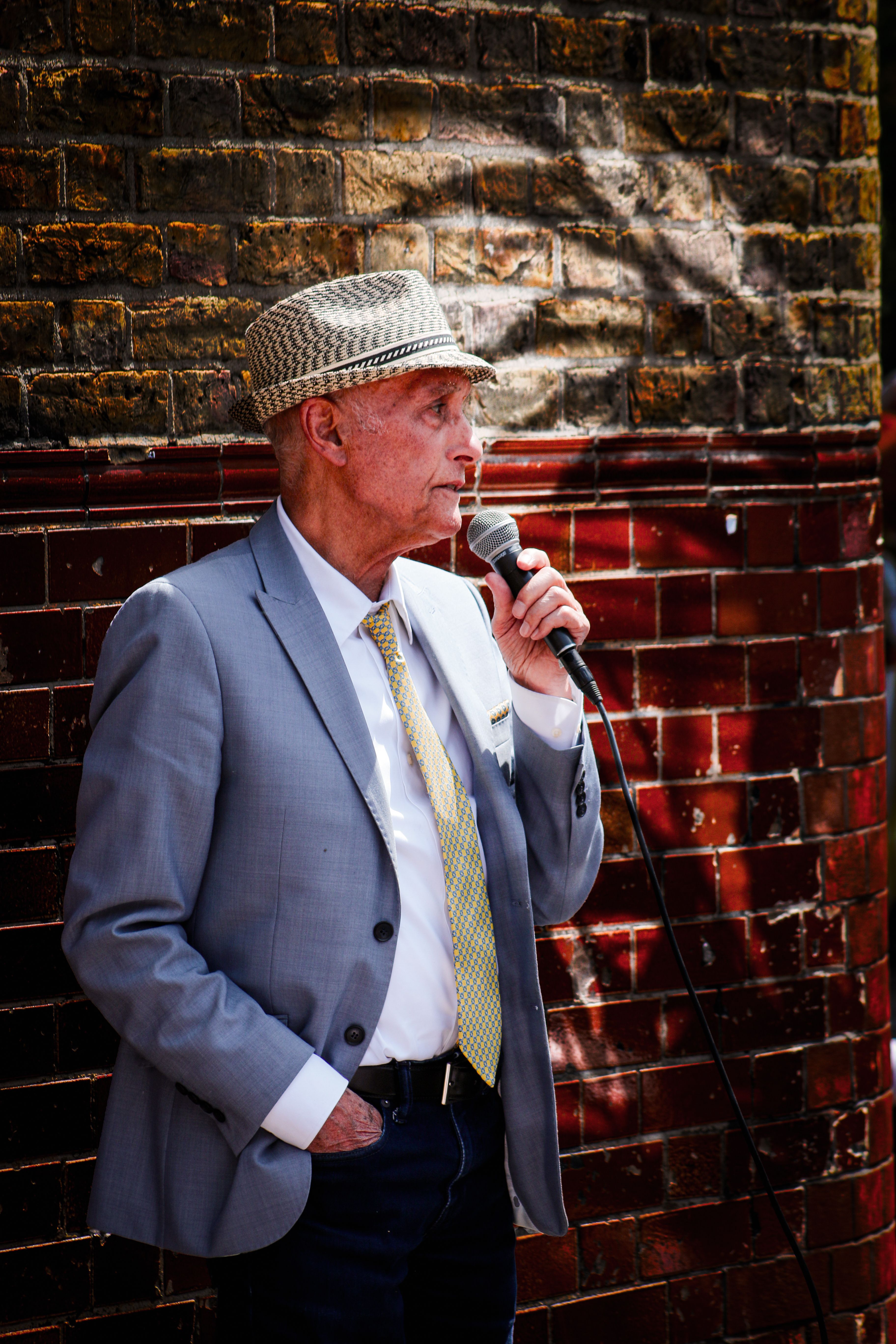 Elderly man in suit performing on a London street with a microphone.