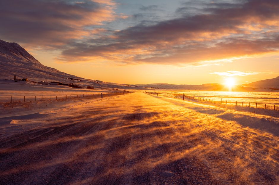 Sunlit snowy rural road in Iceland with a stunning winter sunset scenery.