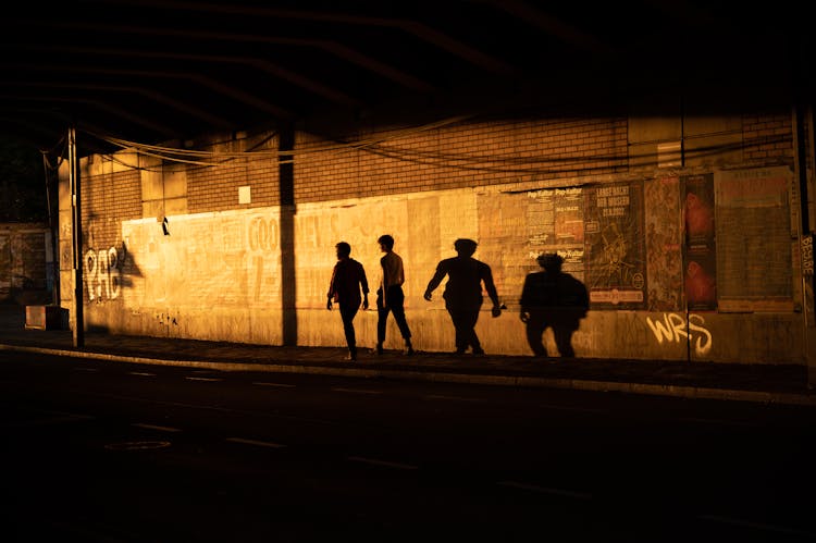 Silhouettes And Shadows Of People Walking On The Sidewalk At Night 