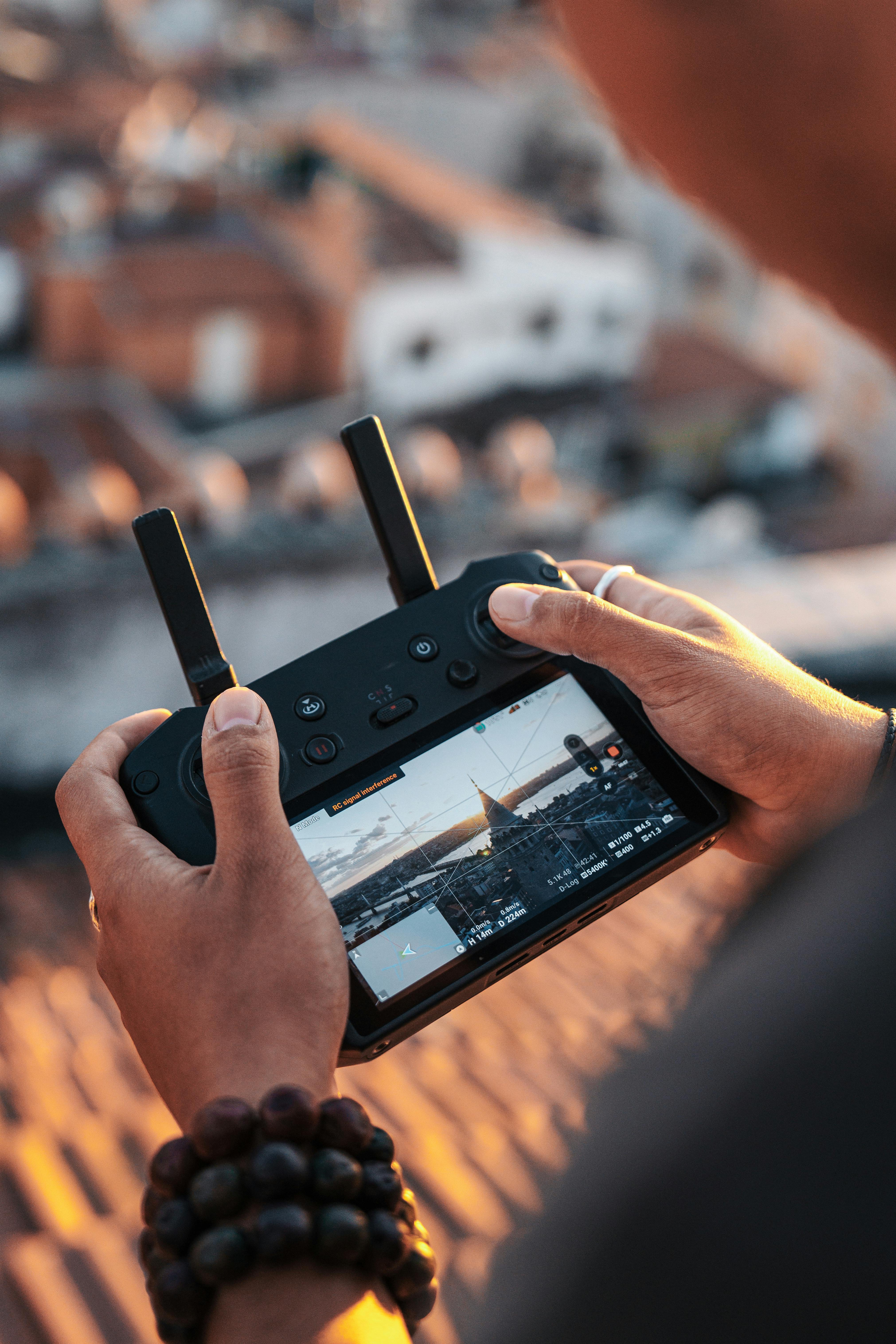 Gratuit Prim-plan al unei persoane care folosește un controler de dronă, surprinzând un peisaj urban la apus. Fotografie de stoc