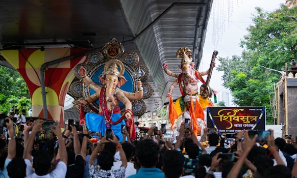 Vibrant scene from Ganesh Chaturthi parade in Mumbai with statues and crowds under a flyover.