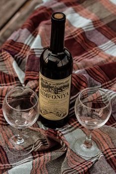 A bottle of red wine with two glasses on a plaid blanket, perfect for a cozy picnic.