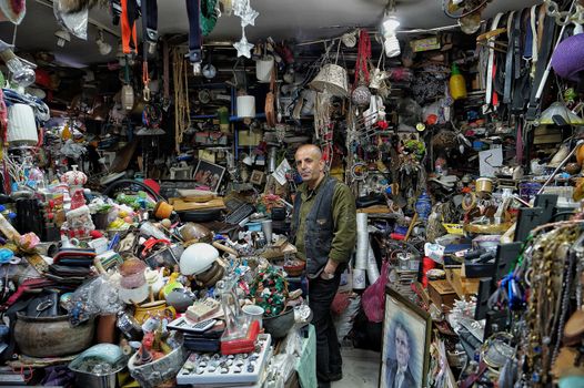 Man standing amidst a cluttered antique shop filled with vintage items.