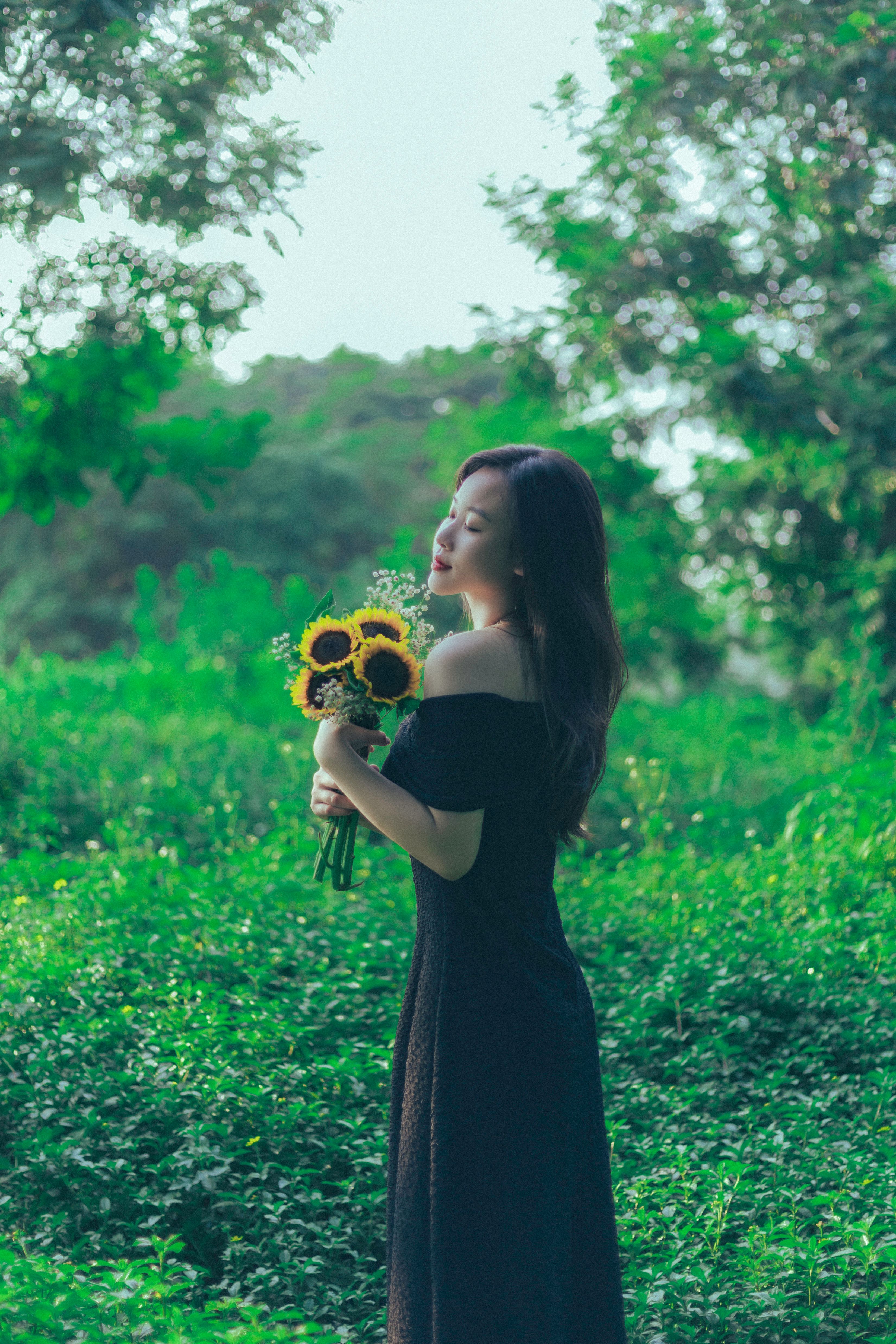 A woman in a black dress holding a bunch of sunflowers  Free Stock Photo