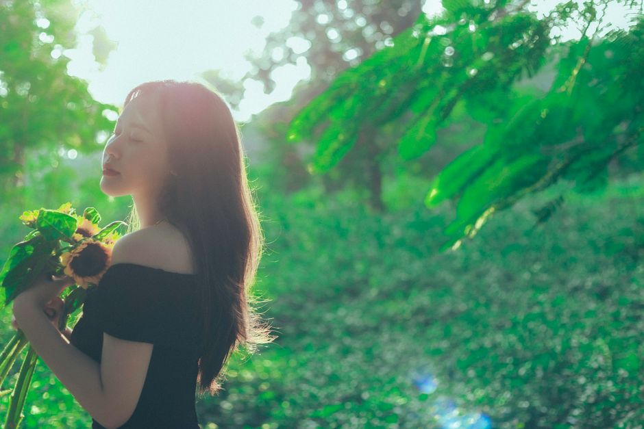 A woman in a serene pose holding sunflowers in a sunlit garden, exuding tranquility.
