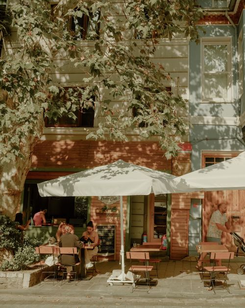 Free Cozy outdoor café scene in Kuzguncuk, Istanbul with people enjoying a meal and shade from umbrellas. Stock Photo