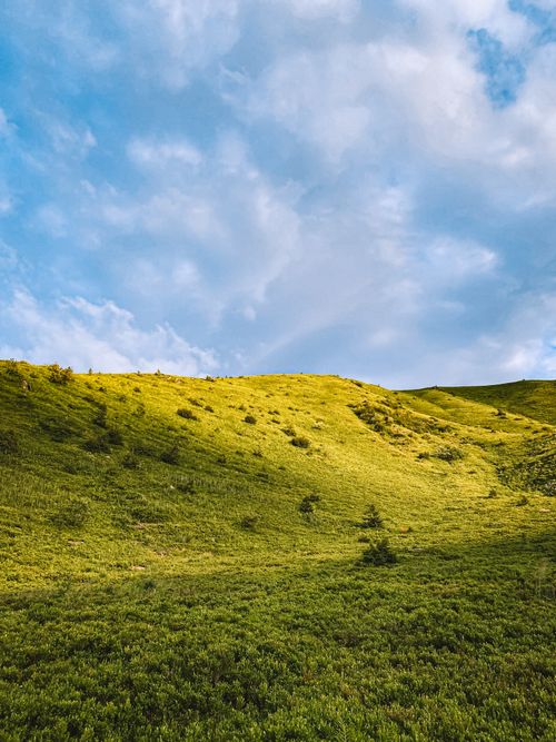 Free Idyllic landscape featuring lush green hills and a bright blue sky with clouds. Stock Photo