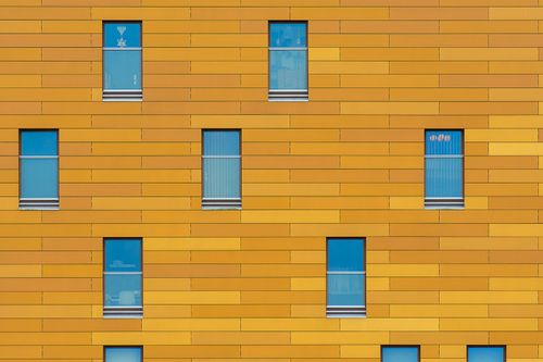 Free Geometric pattern on a yellow building facade with blue glass windows. Stock Photo