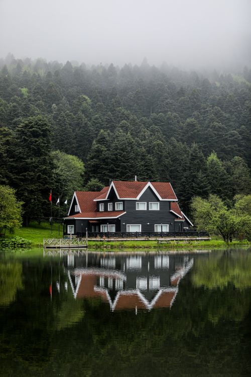Free A tranquil lakeside house with red roof in a misty forest. Perfect serenity. Stock Photo