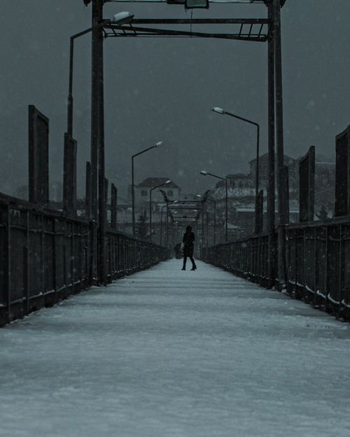 Free A lone figure walks on a snowy bridge in Baku, Azerbaijan at night, creating a dramatic urban silhouette. Stock Photo