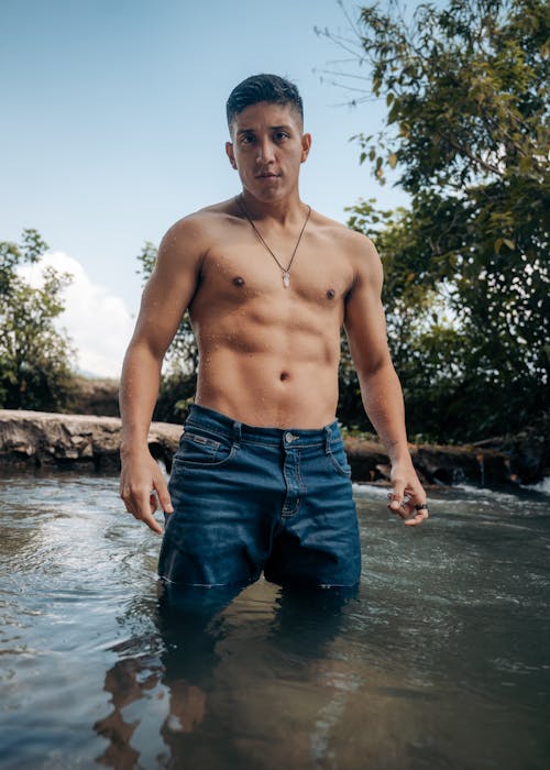 Wet Shirtless Muscular Man in Jeans Standing in River