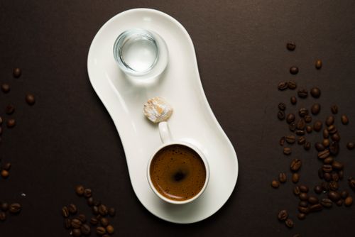 Free Elegant arrangement of Turkish coffee, water, and lokum on a white plate surrounded by coffee beans. Stock Photo
