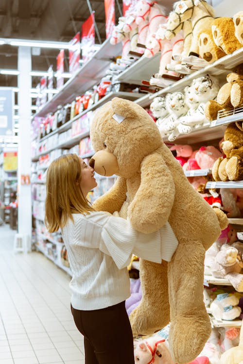 Женщина несет плюшевую игрушку медведя внутри магазина