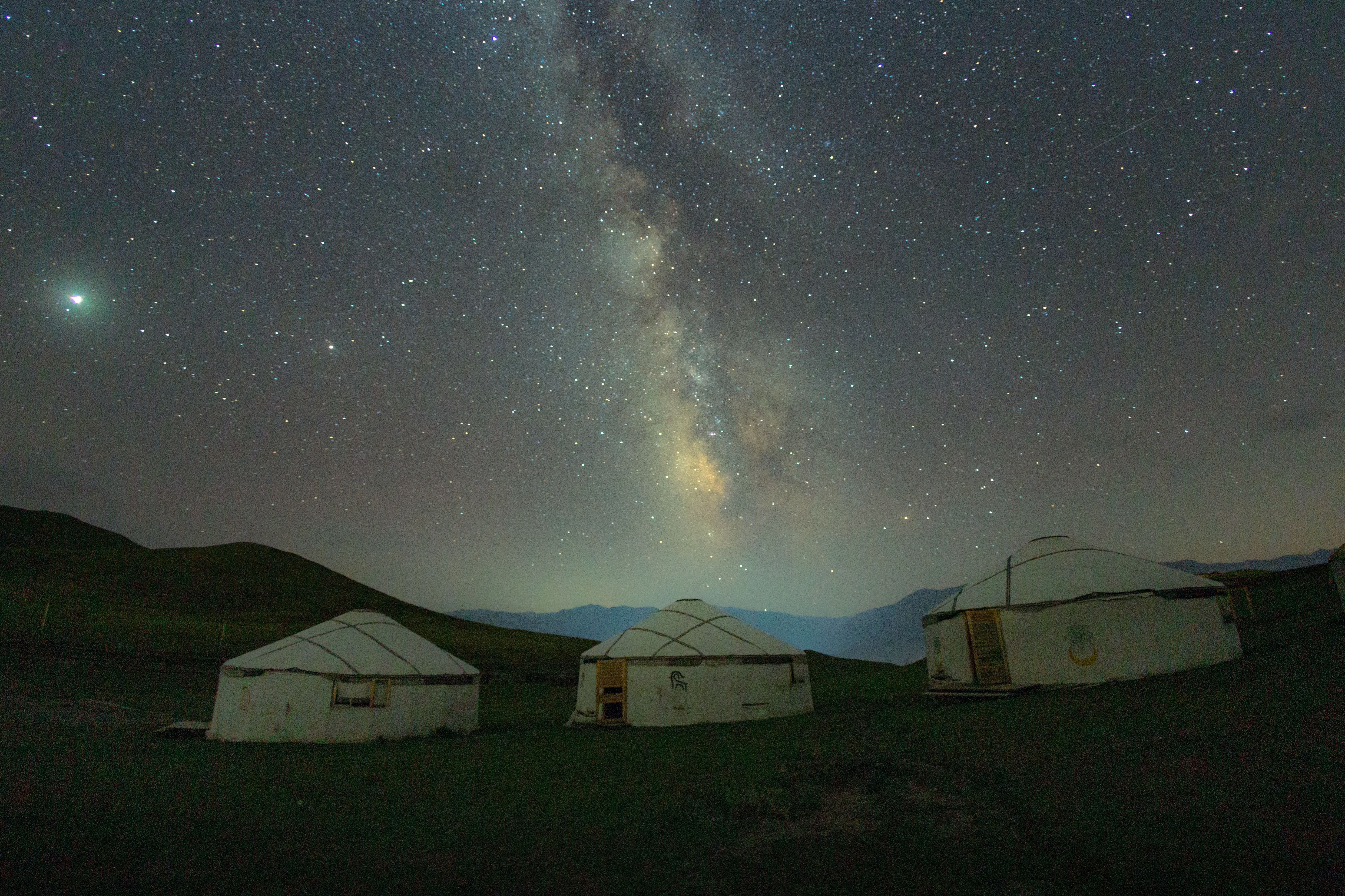 Free Captivating night view of the Milky Way over traditional yurts in a remote, starlit landscape. Stock Photo
