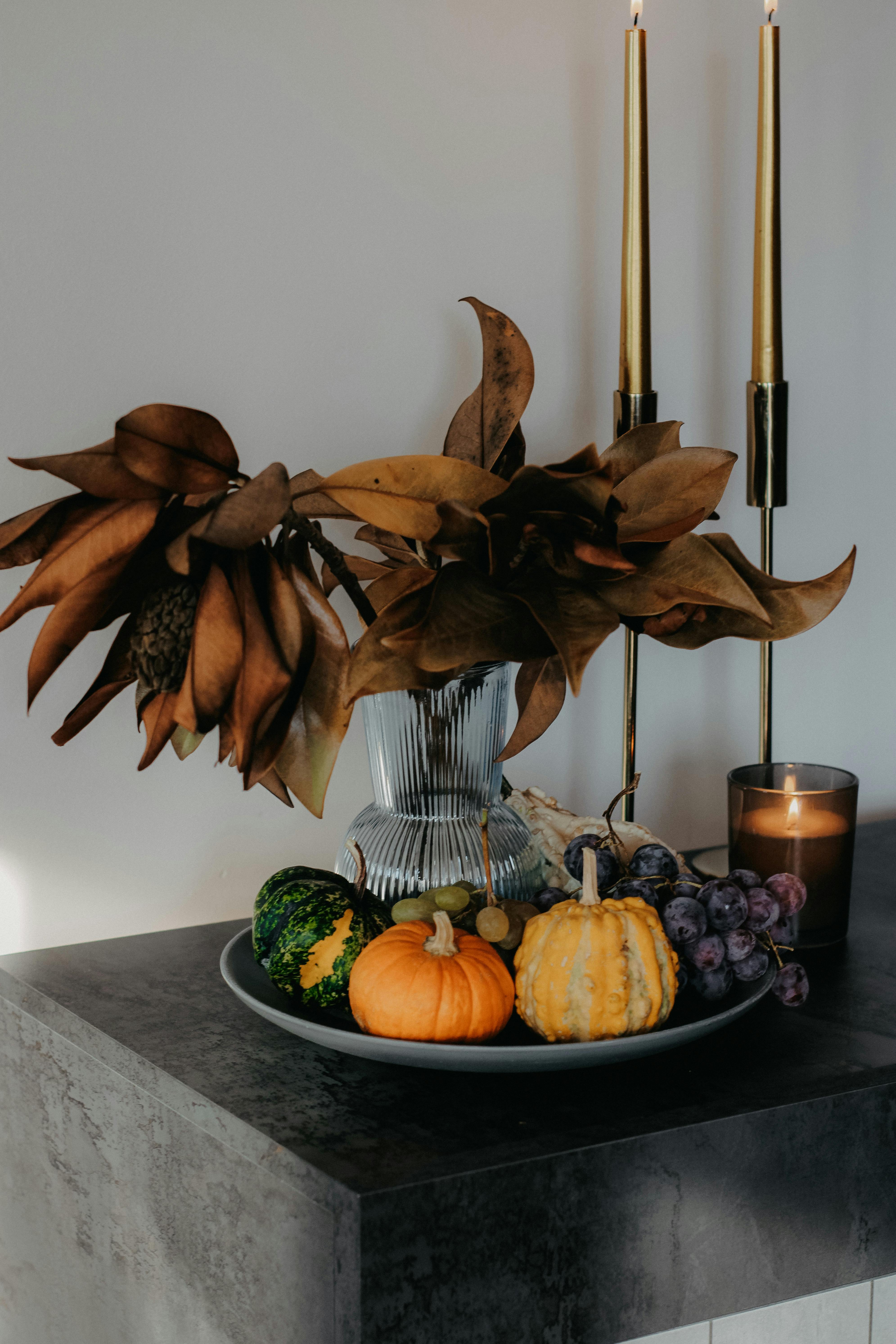 A still life of autumn decor featuring small pumpkins, grapes, and dried leaves indoors.