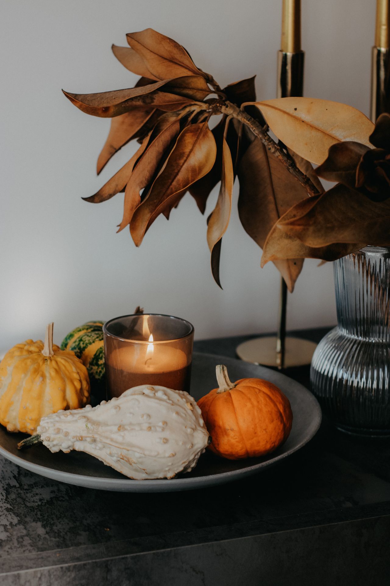 Round tray with small gourds, a lit candle, and dried magnolia leaves