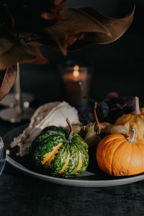 Free Moody autumn still life featuring decorative gourds, grapes, and candlelight on a dark background. Stock Photo