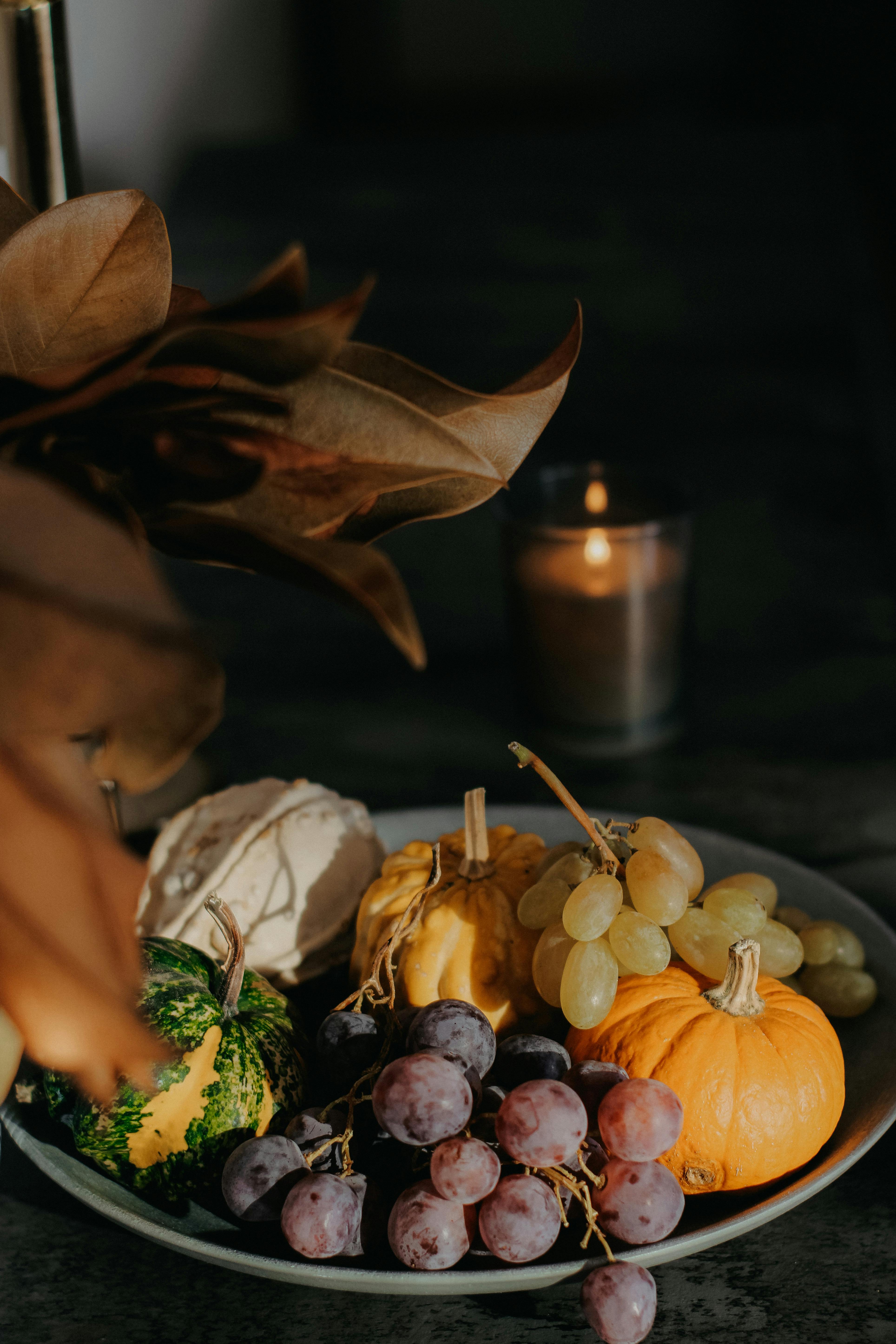 A warm, rustic still life featuring pumpkins, grapes, and a candle, perfect for fall and Thanksgiving themes.