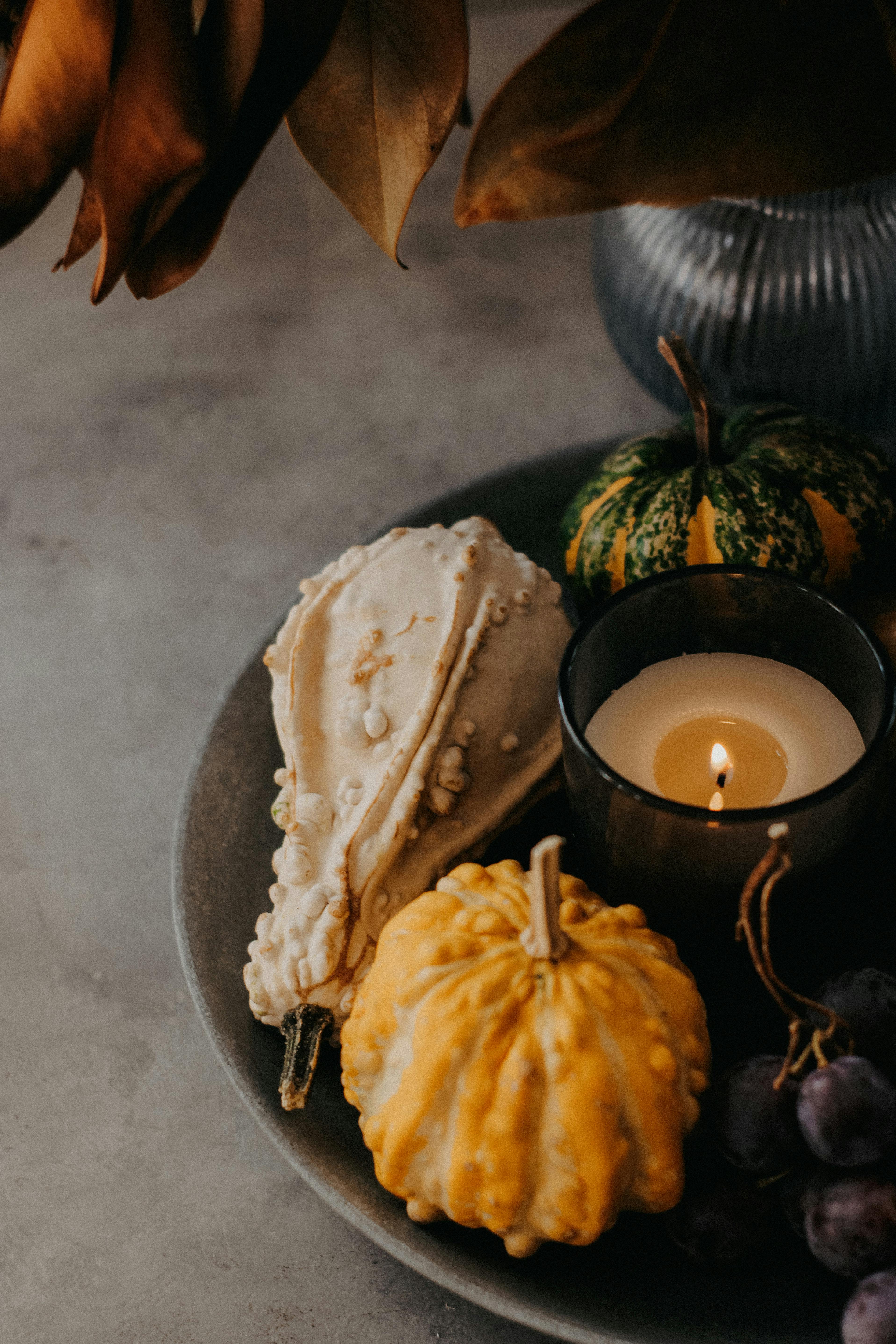 Warm autumn still life featuring decorative gourds and a candle on a rustic surface.