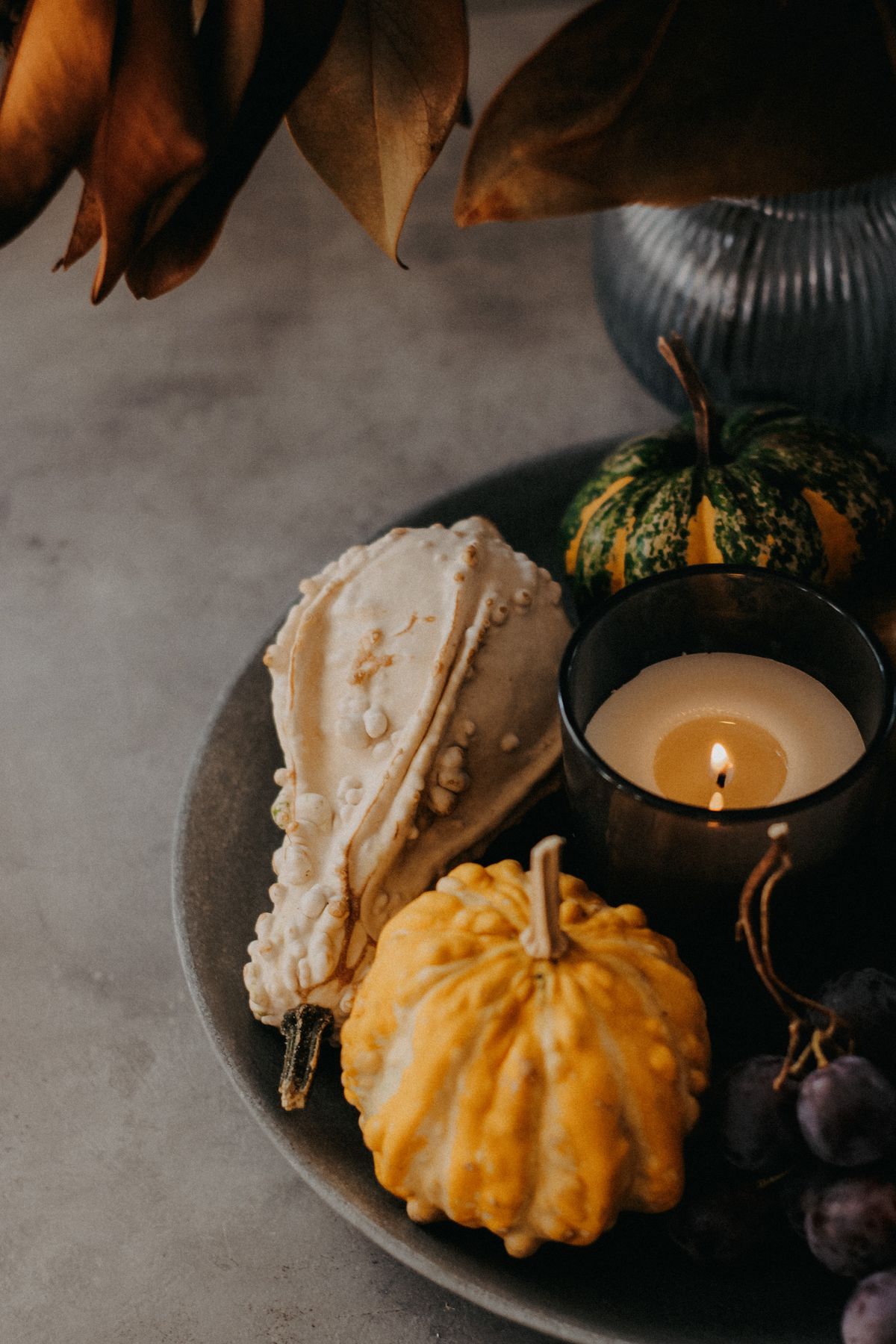 Decorative gourds and a candle arranged on a rustic plate display