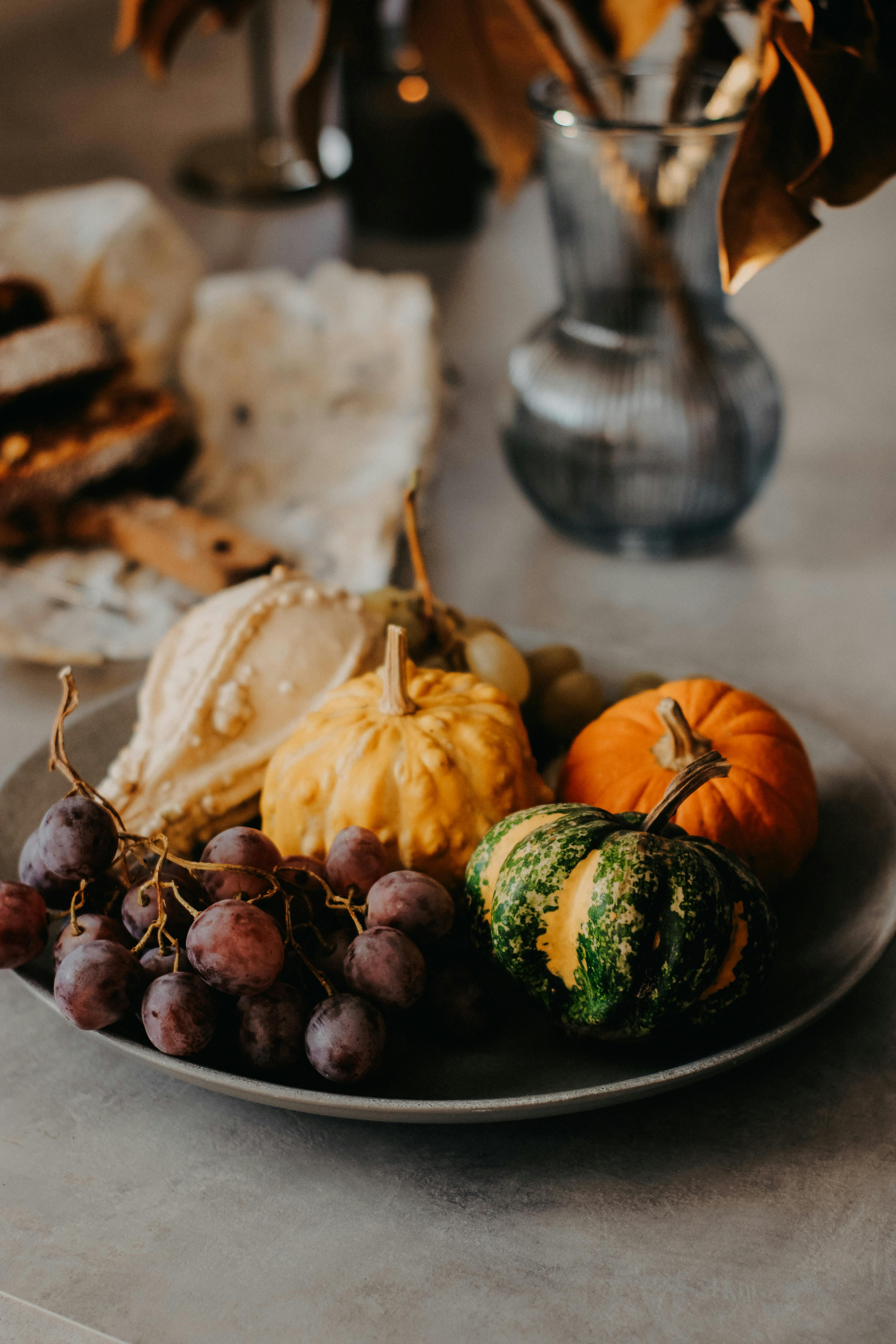 A rustic still life of pumpkins, gourds, and grapes on a table in autumn ambiance.