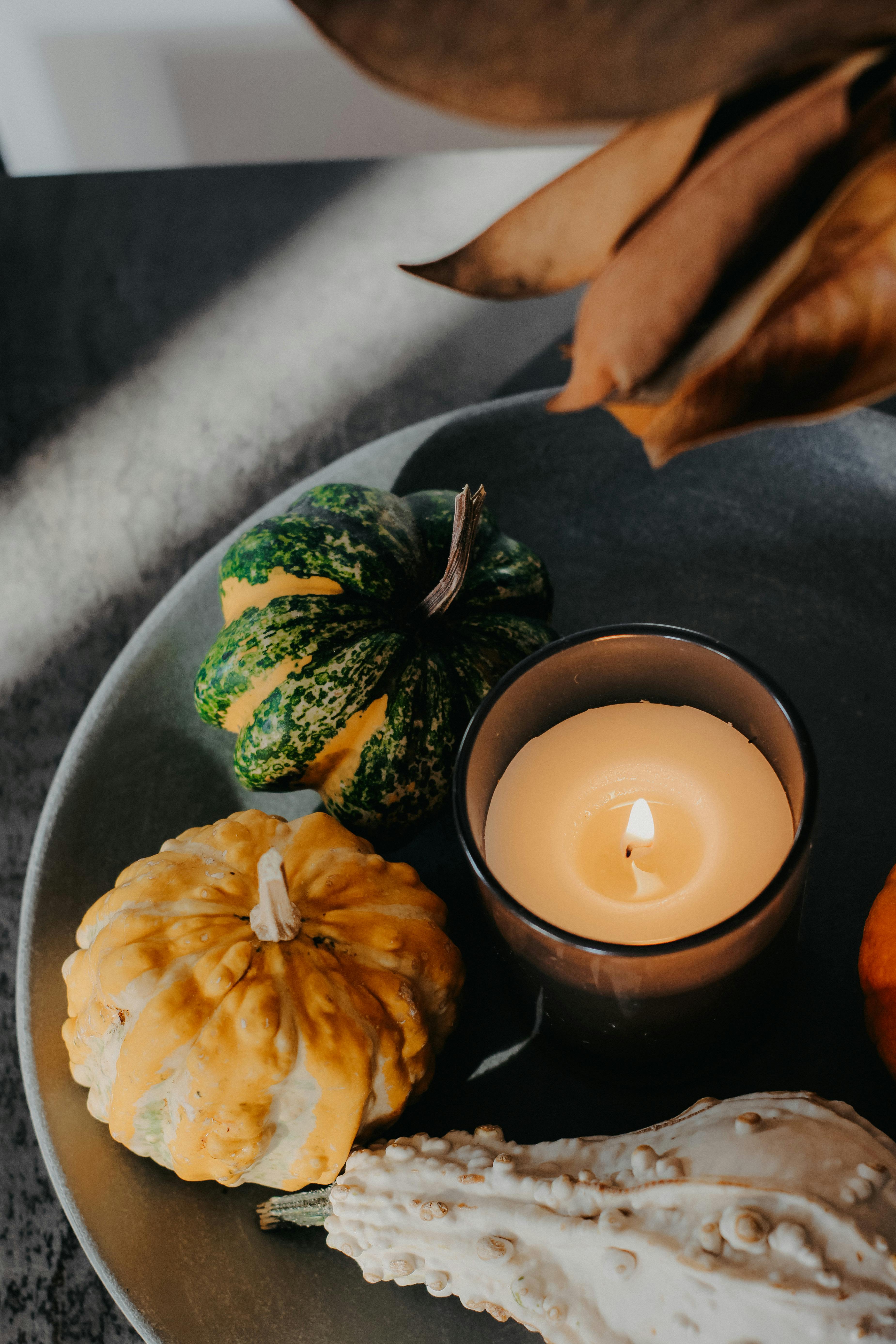 Cozy autumnal setup featuring pumpkins and a lit candle for fall ambiance.