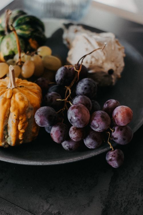 Free A rustic still life of grapes, gourds, and mushrooms on a dark plate. Stock Photo