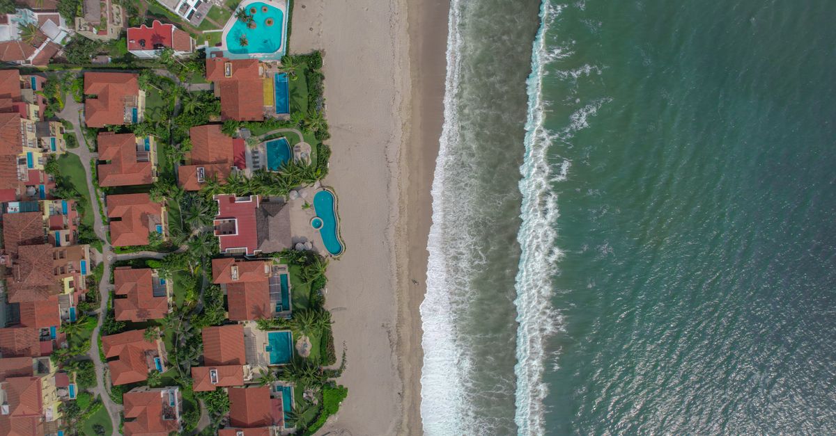 Aerial view of beachfront villas with pools and lush greenery along the shoreline.