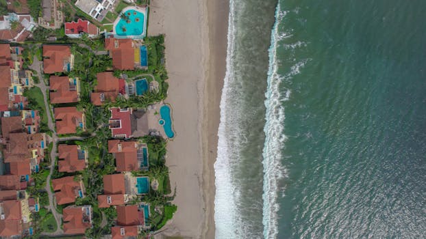 Aerial view of beachfront villas with pools and lush greenery along the shoreline.