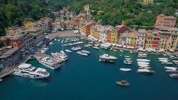 A vibrant aerial view of Portofino's colorful marina bustling with yachts and boats, against a lush hillside backdrop.