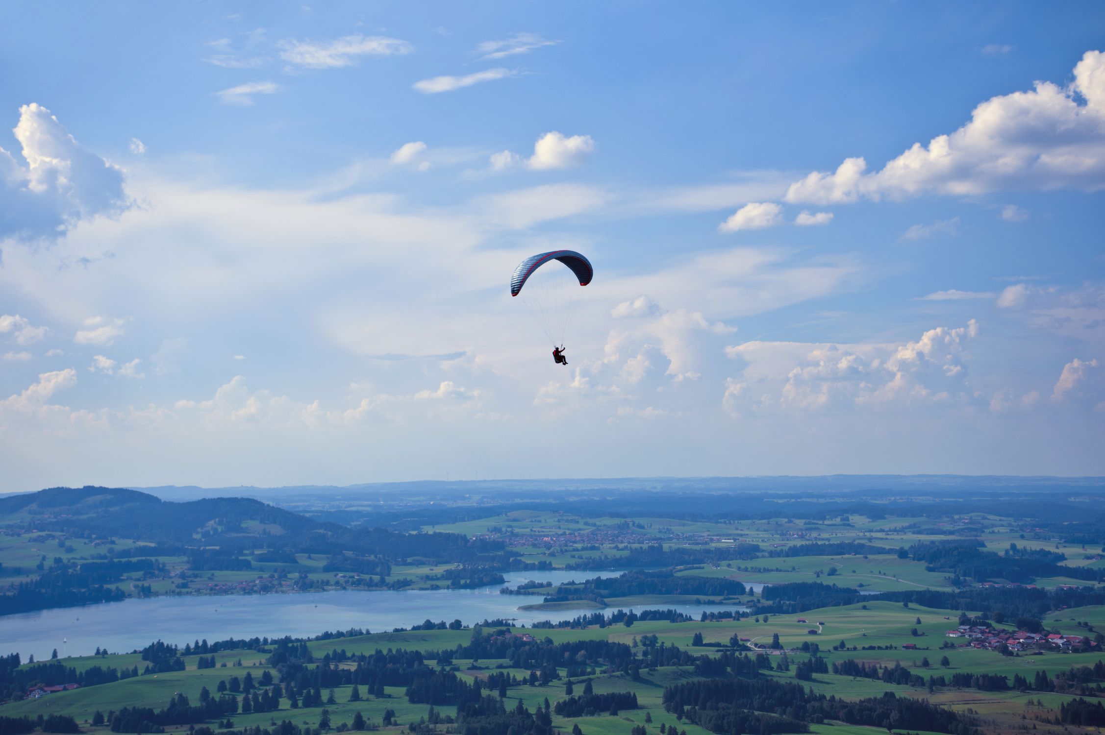 Paraglider soaring above lush green landscapes and lakes in Bavaria Paraglider soaring above lush green landscapes and lakes in Bavaria