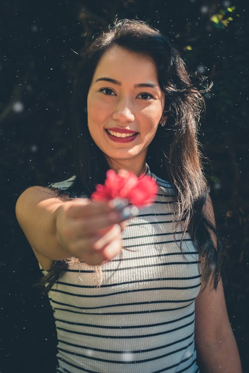 Mujer En Camisa Sin Mangas De Rayas Blancas Y Negras Sosteniendo Flores De Pétalos Rojos Mientras Sonríe