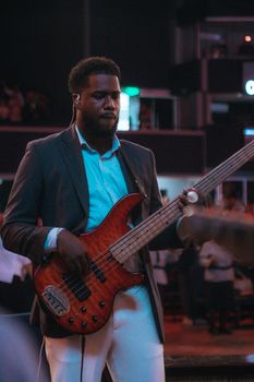 Male bassist performing indoors with vivid lighting and ambient atmosphere.