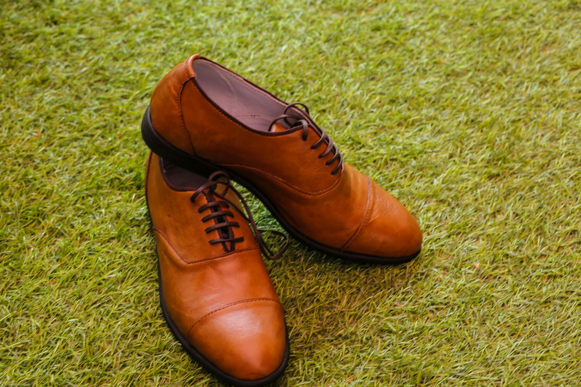 A stylish pair of brown leather oxford shoes elegantly placed on lush green grass.