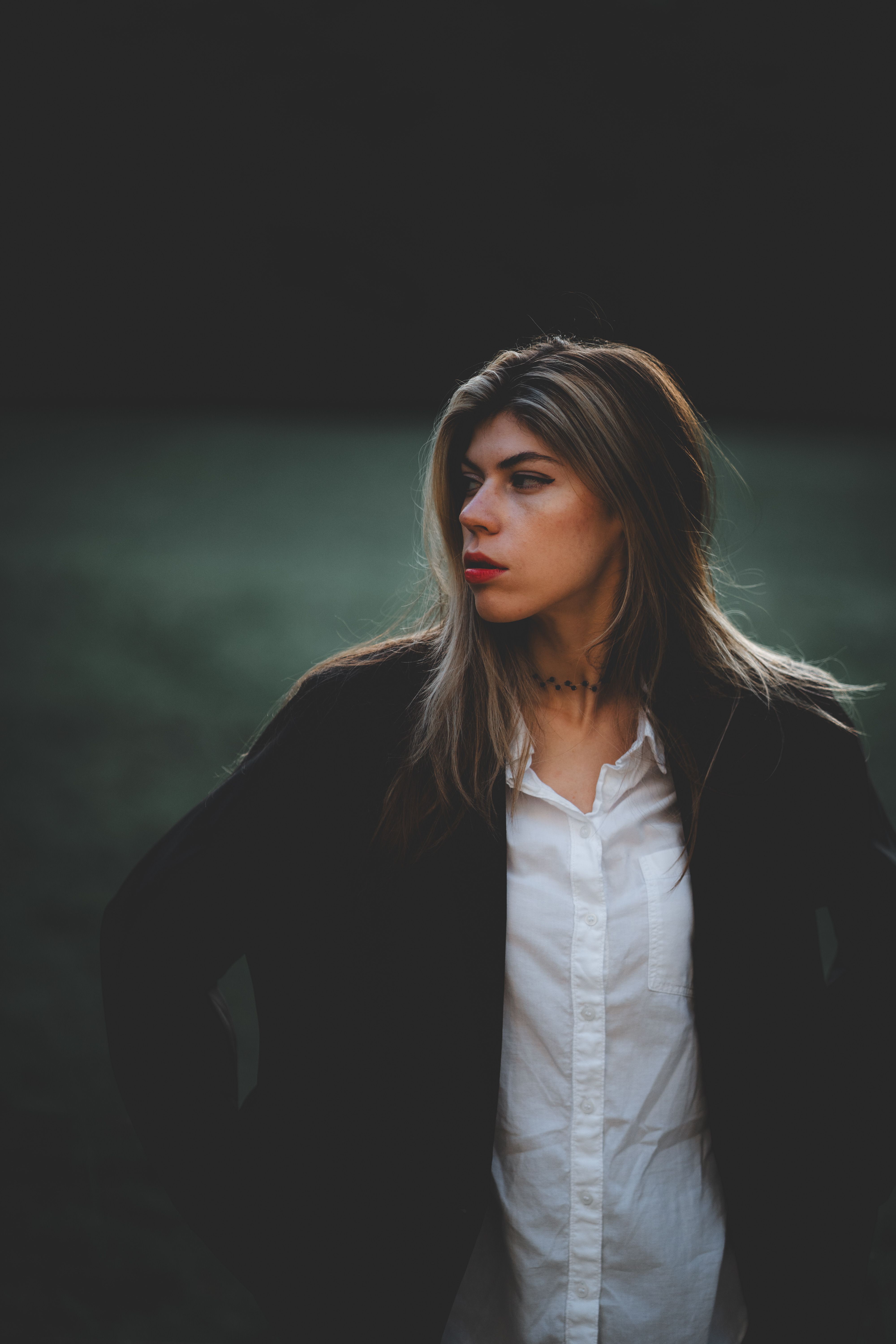 Elegant woman posing in a dark jacket and white blouse in an outdoor evening setting.
