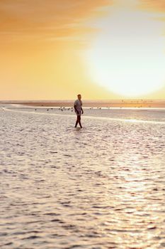 Serene image of a man walking along a beach during a golden hour sunset.