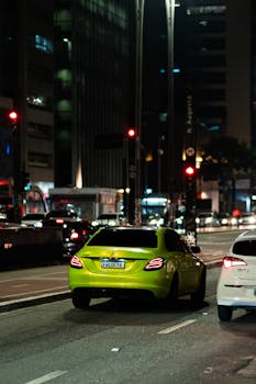 Bright green car navigating the bustling city streets at night, showcasing urban life.