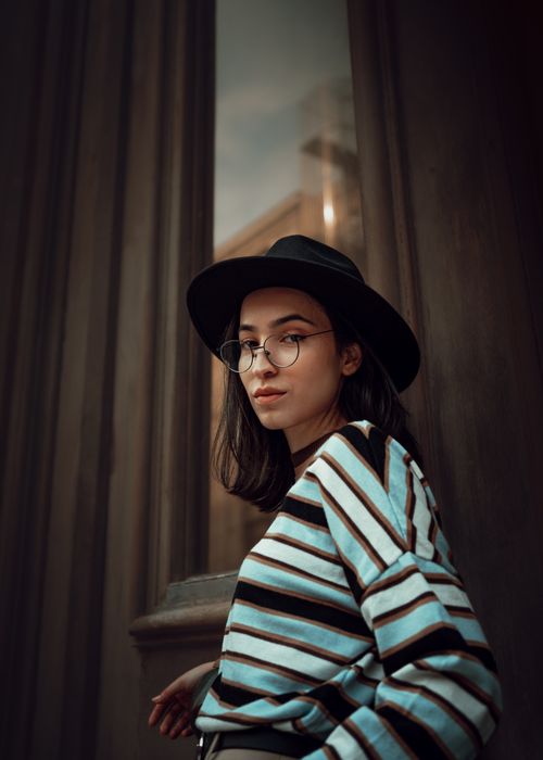 Free Stylish portrait of a young woman wearing glasses and a hat against a textured background. Stock Photo