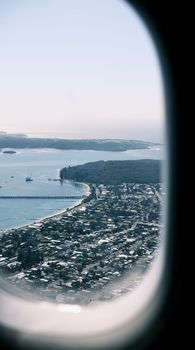 A scenic aerial view from an airplane window shows a coastal city meeting the ocean.